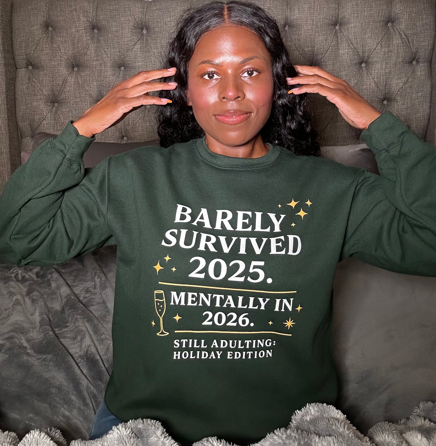 Close-up of Barely Survived 2025 design, Lifestyle photo woman wearing green New Year’s sweatshirt in bedroom