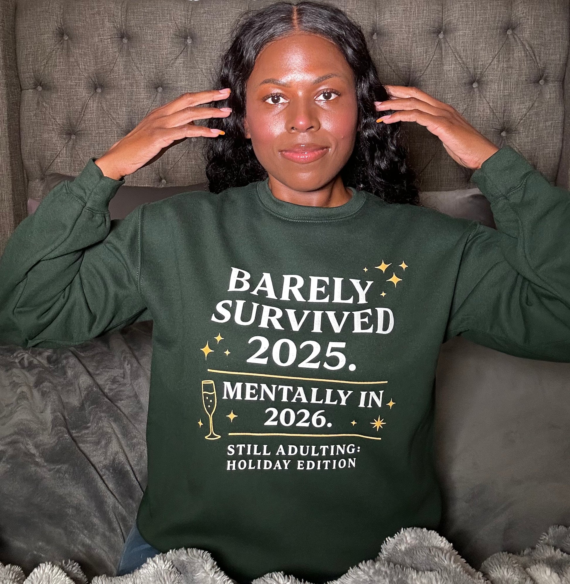 Close-up of Barely Survived 2025 design, Lifestyle photo woman wearing green New Year’s sweatshirt in bedroom