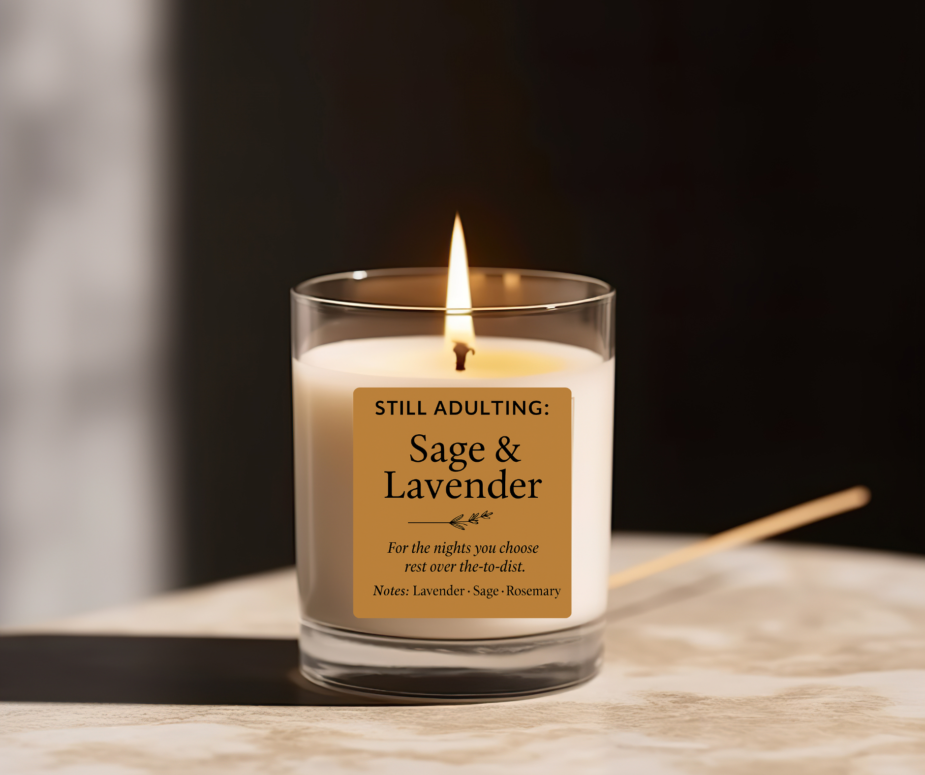 Candle with a label reading 'Still Adulting: Sage & Lavender' on a wooden surface.